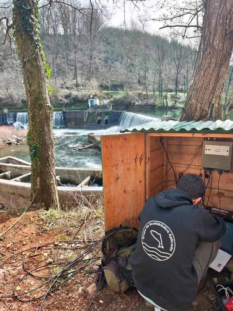 Técnico realizando trabajos de monitorización ecohidráulica junto a un paso para peces y una infraestructura hidráulica en un río.